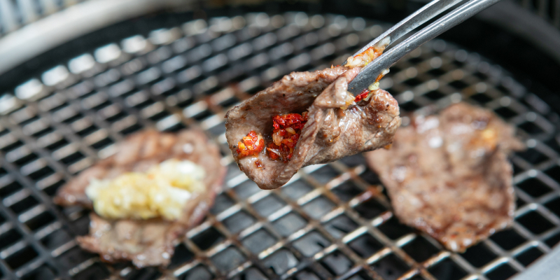 焼けた肉をトングでつまんでいる様子